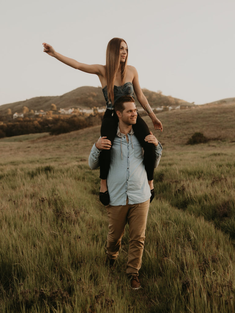A man holds his significant other on his shoulders as they venture through Thomas F Riley Wilderness Park during their engagement shoot with Maya Lora Photo.