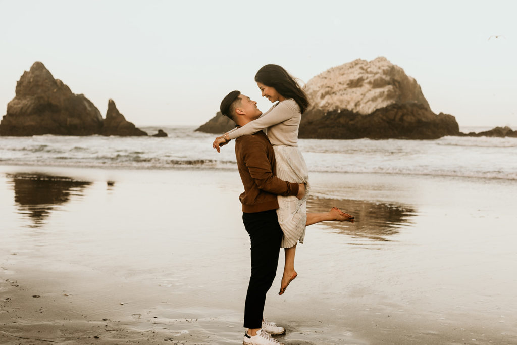 A couple embrace and smile at each other on the shores of Baker Beach